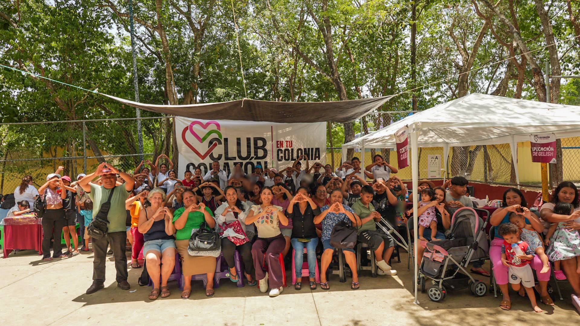 Vecinos y Mirella hacen corazones con las manos bajo la lona de Club Corazón en tu Colonia