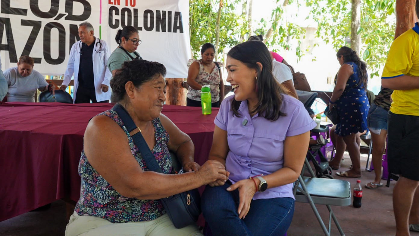 Mirella platica de la mano con una vecina en la mesa de servicios de una brigada