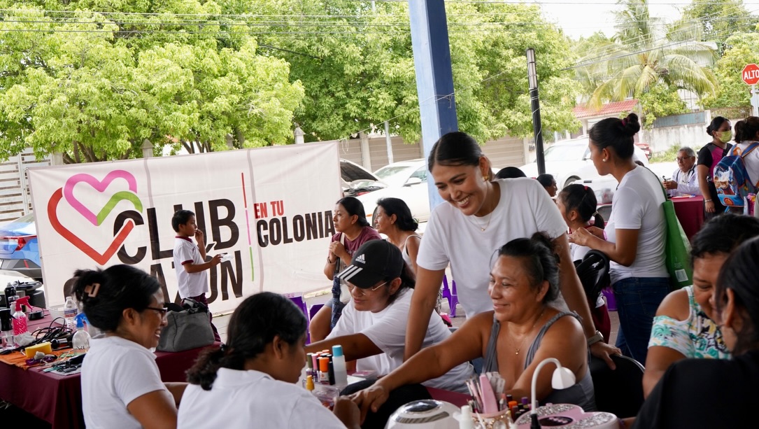 Mirella ríe con vecinas en la mesa de servicio de una brigada, con la lona de Club Corazón en tu Colonia detrás